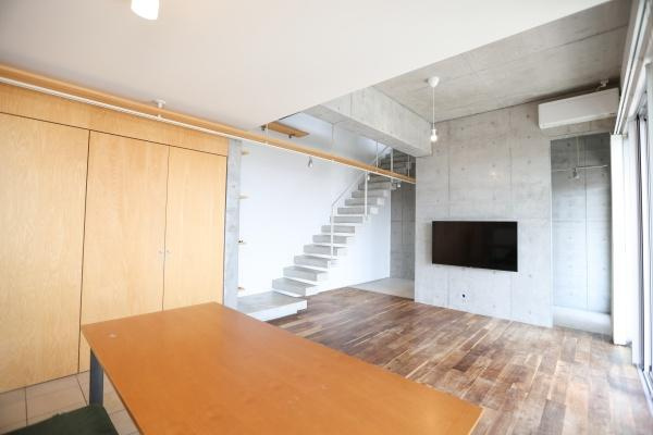 青葉台　戸建ての居間・リビング|コンクリート打ちっぱなしの壁が印象的なリビングです。大きな窓から光が差し込み明るい空間を演出しています。壁付けのテレビやスタイリッシュな階段が現代的な雰囲気を引き立てます。