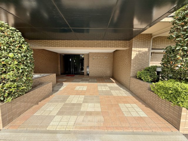 グランドクレスト清瀬のエントランス|鮮やかな緑の植栽と、落ち着いたブラウン系のタイル張りのアプローチが、住まいの顔として上質な雰囲気を演出します