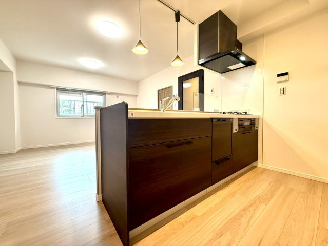 メゾンドール多摩川のキッチン|ダークブラウンの面材が印象的なシステムキッチン。食洗機・三口コンロを備え、機能美とデザインを両立しています。