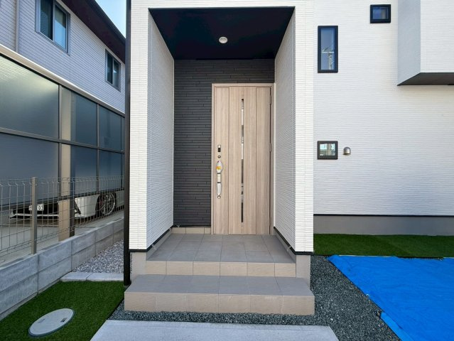 高知市高須3期2棟 2号棟の玄関|木目ドアと黒の外壁が印象的な玄関ポーチ。モノトーンの中に温もりを感じる、上品なデザインです