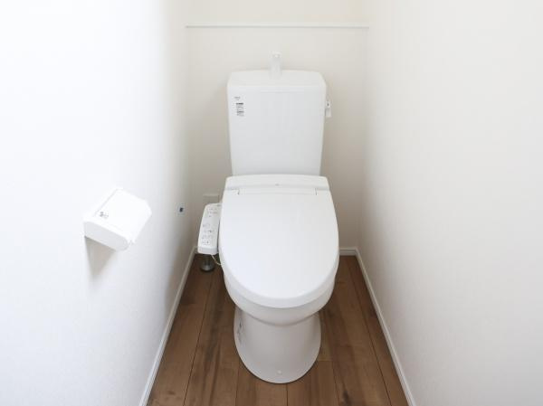 横尾東町2丁目2期1号棟のトイレ|白を基調とした清潔感のあるトイレです。床は木目調で温かみのある雰囲気が感じられます。シンプルなデザインでお手入れも簡単です。壁面が広く圧迫感を軽減しています。