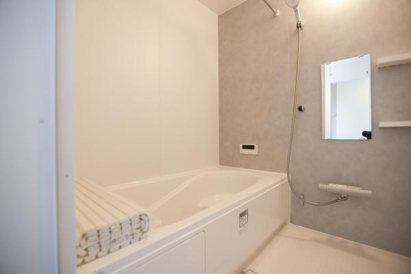 横尾東町2丁目2期2号棟の浴室|明るい色合いで統一されたバスルームです。シャワーと浴槽が使いやすいレイアウトになっています。鏡や棚が設置されていて日々の使い勝手も考えられています。シンプルで清潔感のある空間が魅力です。