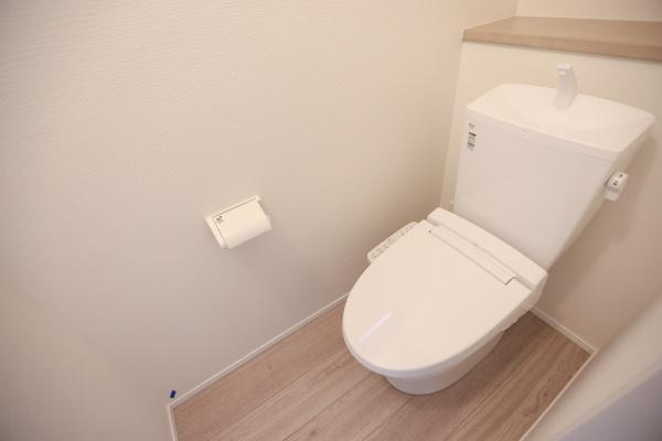 横尾東町2丁目2期2号棟のトイレ|明るい色合いの床材と壁がトイレ空間をすっきりとした印象にしています。タンク一体型のデザインでお手入れしやすい形状です。ペーパーホルダーが使いやすい位置に設置されています。