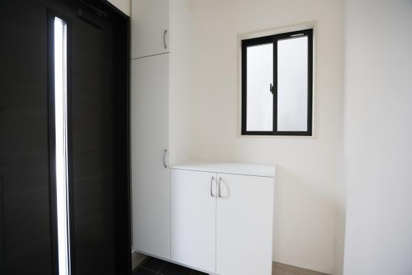 横尾東町2丁目2期2号棟の玄関|明るい窓がある玄関で収納スペースも備え付けられています。白を基調としたデザインが空間をすっきりと見せます。扉のスリットから光が入りやすい設計です。ゆとりのあるレイアウトが印象的です。