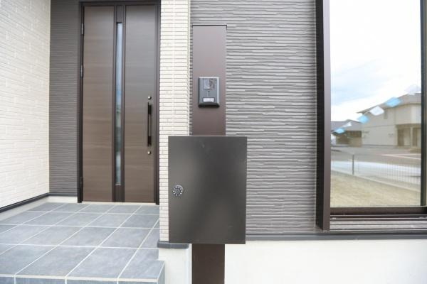 横尾東町2丁目2期2号棟の玄関|落ち着いた色合いの玄関ドアが印象的です。タイル貼りのアプローチがすっきりとした印象を与えます。大型の窓が隣接しているため明るい雰囲気が感じられる玄関です。