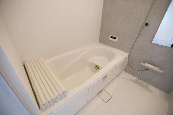 横尾東町2丁目2期2号棟の浴室|ゆったりとしたバスタブが特徴でお手入れしやすいシンプルなデザインです。壁面のモノトーンカラーが落ち着いた印象を与えます。手すりや浴室用フタが備わっており使い勝手にも配慮されています。