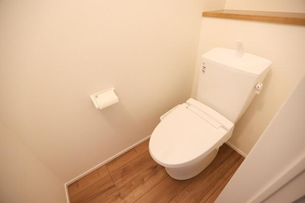 横尾東町2丁目2期3号棟のトイレ|温かみのある木目調の床が印象的です。清潔感あふれるホワイトのトイレ本体が配置されています。壁面がシンプルで落ち着いた空間を演出しています。ペーパーホルダーも使いやすい位置に設置されています。