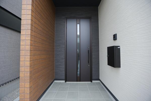 横尾東町2丁目2期3号棟の玄関|玄関はモダンなデザインで落ち着いた色合いが特徴です。広々としたスペースが来客時にも便利です。雨の日でも安心な屋根付きのアプローチが魅力です。スタイリッシュな印象を与えます。
