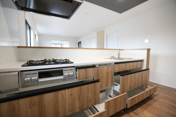 横尾東町2丁目2期3号棟のキッチン|スタイリッシュなデザインのキッチンです。収納スペースが豊富で使い勝手が良さそうです。ガスコンロとシンクが使いやすい位置に配置されています。木目調の扉が温もりを感じさせます。