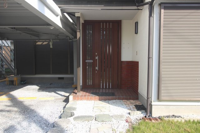 小山市犬塚の玄関|木目調の玄関ドアが温かみのある印象を与えてくれます。屋根付きのアプローチで雨の日でも濡れにくく、落ち着いたタイル敷きが来客をやさしく迎えてくれます。