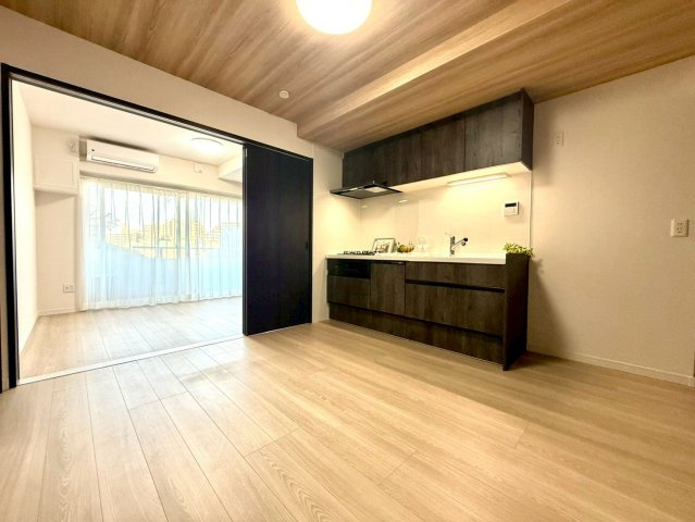 セザールたまプラーザの居間・リビング|木目天井とダークブラウンのキッチンが調和する、落ち着いた雰囲気のLDK。引き戸を開けることで空間が一体となり、広々とした住まい方が叶います。