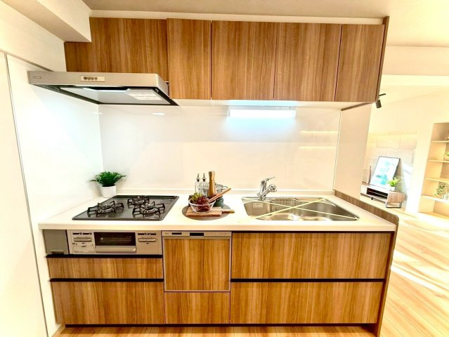 扶桑ハイツ南太田のキッチン|木目調パネルとホワイト天板が美しく調和したシステムキッチン。三口コンロ・十分な収納を備え、毎日の料理が気持ちよくはかどります。