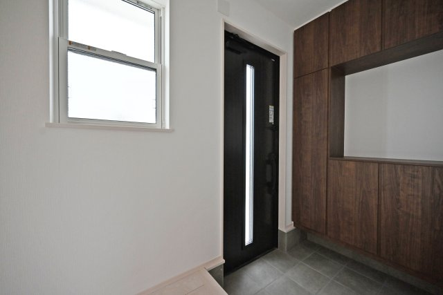 ファーストタウン荻野3丁目新築一戸建て│2SLDK・3SLDK+駐車2台可の玄関|1階玄関を廊下側から撮影した内観写真です。 
シンプルな玄関扉にシューズボックス、小窓を配置したオーソドックスな玄関です。