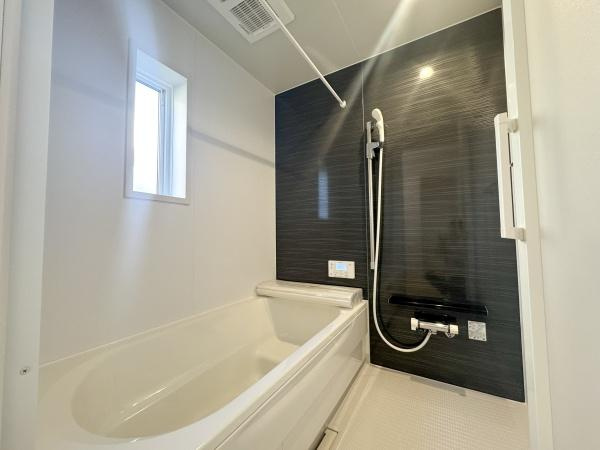 徳島第7-1号棟の浴室|窓付きのバスルームは明るく換気もスムーズに行えます。ダークトーンのアクセントパネルが落ち着いた雰囲気を演出しています。手すり付きの設計で出入りも安心です。シンプルで機能的な空間が特徴です。