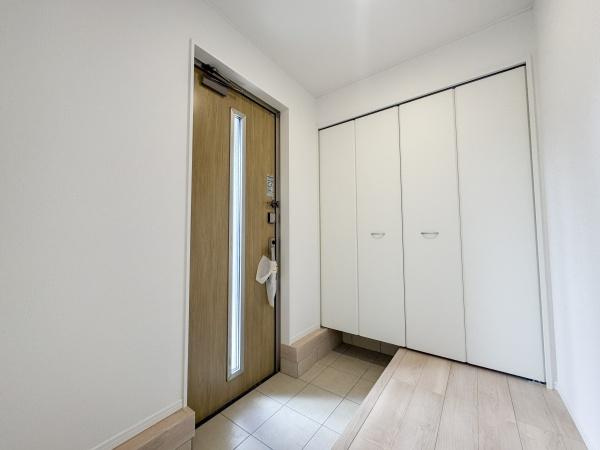 徳島第7-1号棟の玄関|明るい木目調の玄関ドアが印象的です。収納スペースがしっかり確保されていてすっきりとした空間です。白を基調とした内装で清潔感が感じられます。室内と玄関に段差があり使いやすい動線設計です。