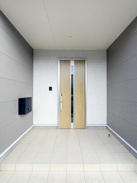徳島第7-1号棟の玄関|すっきりとしたデザインの玄関が印象的です。明るいタイル使いが入口を広々と演出しています。木目調のドアが落ち着いた雰囲気を醸し出しています。モダンな外観が特徴的です。