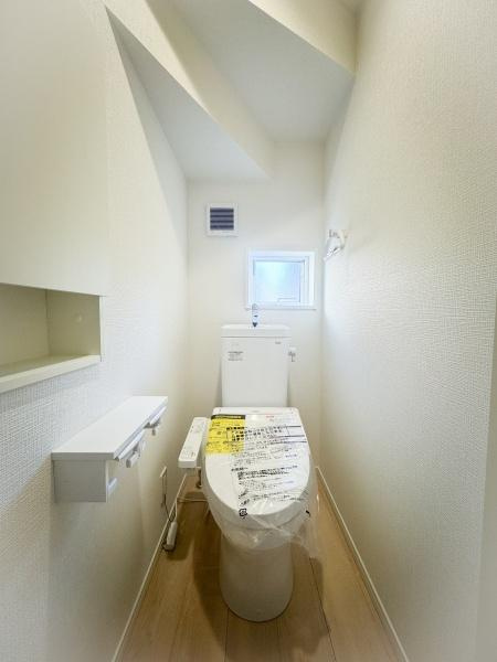 畑中第1-2号棟のトイレ|窓付きで自然光が入るトイレです。棚やペーパーホルダーも設置されており収納性に配慮されています。シンプルな内装で清潔感があります。換気口も設けられ快適にお使いいただけます。