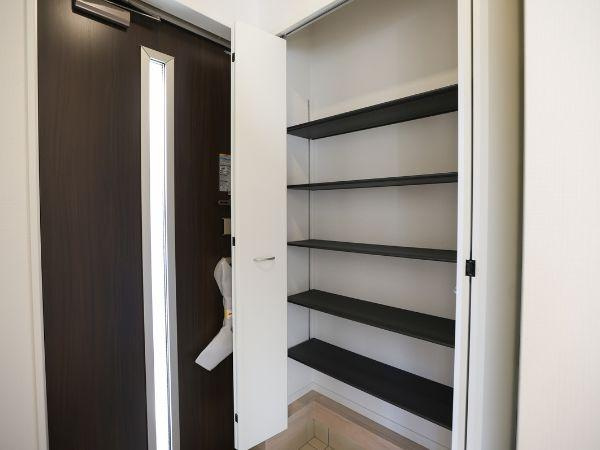 横田第2-2号棟の玄関|玄関には収納スペースが設けられており実用的な設計です。棚が複数あり使い分けに便利です。玄関ドアはスリット付きで採光も考慮されています。清潔感のある空間が広がります。