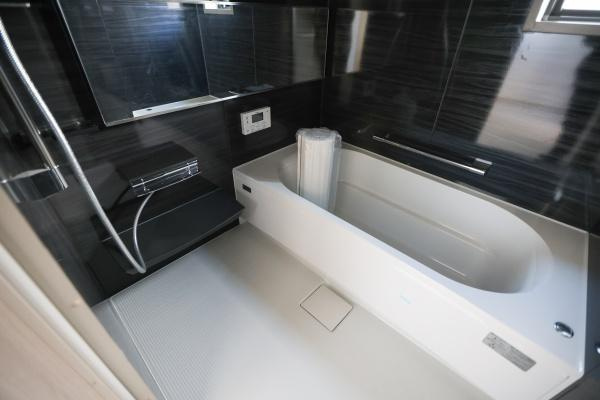 AG-HOUSE　ゆめが丘　A棟の浴室|落ち着いた色合いの壁面が上品な浴室です。広々としたバスタブが設けられています。収納スペースや洗い場も付いており使い勝手の良さが感じられます。