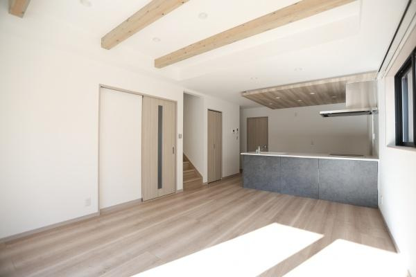 AG-HOUSE　ゆめが丘　A棟の居間・リビング|大きな窓からたっぷりと自然光が入る明るいリビングです。天井の梁が空間にアクセントを加えています。キッチンとの一体感があり開放的な印象を受けます。床材や建具の色味が統一され落ち着いた雰囲気です。