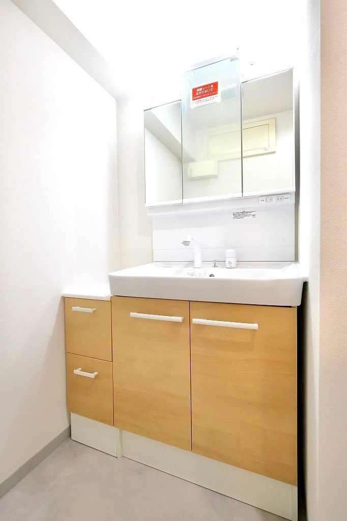 モリスガーデンヒルズ井土ヶ谷の独立洗面台|三面鏡付きで収納力も豊富な洗面台。明るい木目の扉が柔らかな印象を与え、朝の身支度が快適に行えるスッキリとした洗面スペースです。