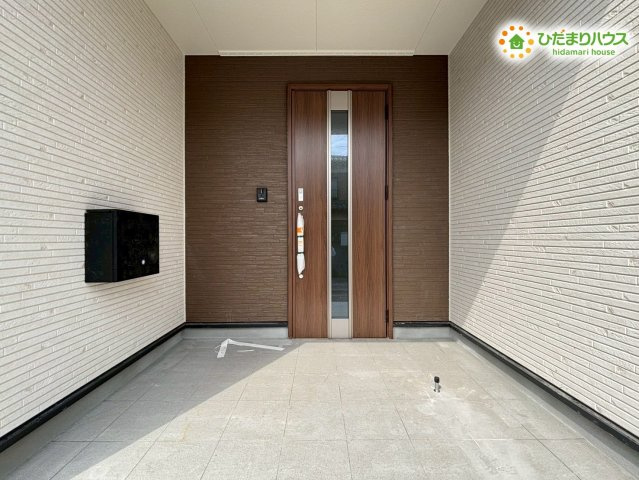 鴻巣市箕田　第9　新築一戸建て　クレイドルガーデン　01の玄関|屋根のある設計で、雨の日でも濡れずに鍵を開け閉めできる玄関ポーチです！落ち着いた木目調のドアが明るい外壁に映え、自宅へ戻るたびに心がホッと休まるような雰囲気が演出されていますね♪