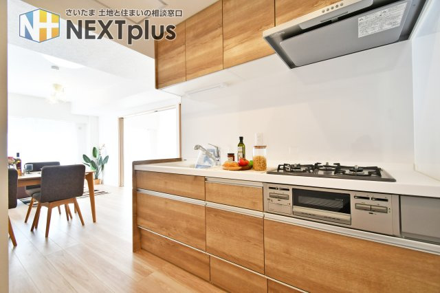 ライネスハイム東浦和のキッチン|木目基調の吊戸棚付きシステムキッチンです。上にも下にもたくさん収納出来ますので、別途で食器棚がなくてもたくさん収納する事ができます！ライトもありますので、お料理中の手元もしっかり照らしてくれます。