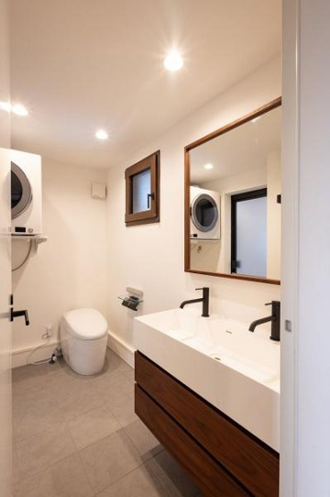 【独立洗面台】 | 明るい照明と大きな鏡が特徴的で空間が広く感じられます。シンプルな内装で清潔感があります。窓からの採光があり換気もしやすい仕様です。無駄のないレイアウトで動線もスムーズです。