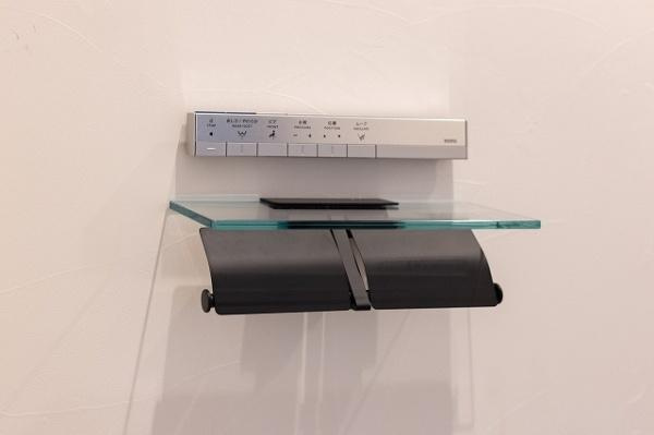 【トイレ】 | 壁付けの操作パネルとガラス棚が設置されておりシンプルなデザインが空間を引き締めます。ペーパーホルダーは2連式で使いやすさも意識されています。ムダのない造りで清潔感のある仕上がりです。収納棚も便利です。