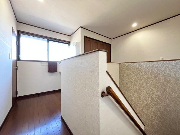 判田台南3丁目　戸建の内装|階段ホールには落ち着いた木目調の床が施されシンプルな内装が印象的です。明るい窓から光が差し込む空間には使いやすい収納スペースも確保されています。手すりが備わっていて安全面にも配慮されています。