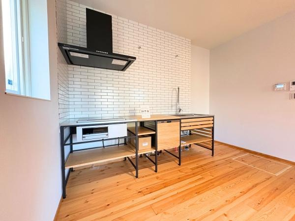 つのこばるヴィレッジ　Ｂ棟のキッチン|明るい木目の床と白いタイル壁が調和したキッチンです。シンプルなデザインで空間が広く感じられます。収納スペースも確保されており使い勝手にも配慮されています。