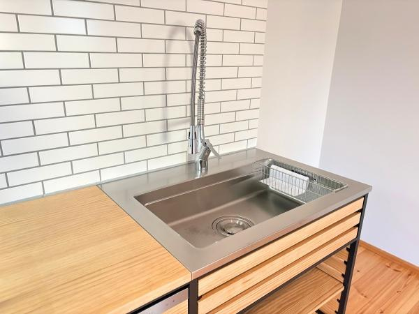 つのこばるヴィレッジ　Ｂ棟のキッチン|シンプルなデザインのキッチンシンクが印象的です。タイル張りの壁面が清潔感を演出しています。使いやすい蛇口とステンレス天板はお手入れも簡単です。木材のカウンターが温かみを添えています。