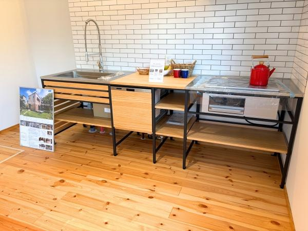 つのこばるヴィレッジ　A棟のキッチン|開放感のあるシンプルなキッチンです。ホワイトのタイル壁と木の床の組み合わせが調和しています。オープンシェルフのデザインで整理整頓がしやすい印象です。