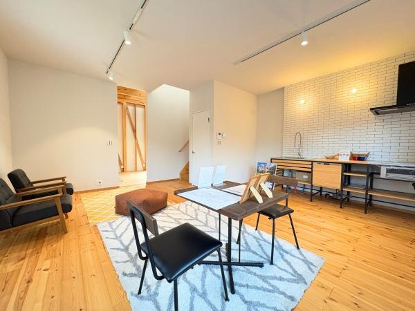 つのこばるヴィレッジ　A棟の居間・リビング|木目が美しいフローリングが広がる開放感のある空間です。白い壁と明るい照明が室内をより一層明るく見せています。シンプルなデザインのキッチンが印象的です。