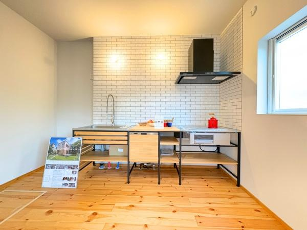 つのこばるヴィレッジ　A棟のキッチン|白いタイルの壁とシンプルなデザインが印象的なキッチンです。開放感のある空間で広々とした木目調のフローリングが特徴です。収納スペースも確保されています。