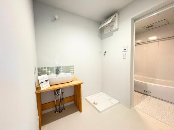 つのこばるヴィレッジ　A棟の独立洗面台|洗面台にはシンプルなデザインの洗面ボウルが設置されています。空間にはナチュラルな雰囲気が広がり壁にもアクセントのタイルが施されています。洗濯機置き場も確保されておりバスルームへの動線も短く便利です。