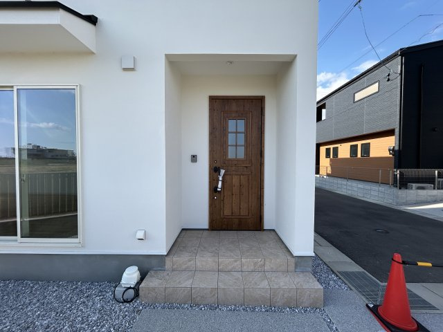 南国市大そね甲　新築一戸建ての玄関|白い塗り壁に格子窓のついた木目のドアが映えます。