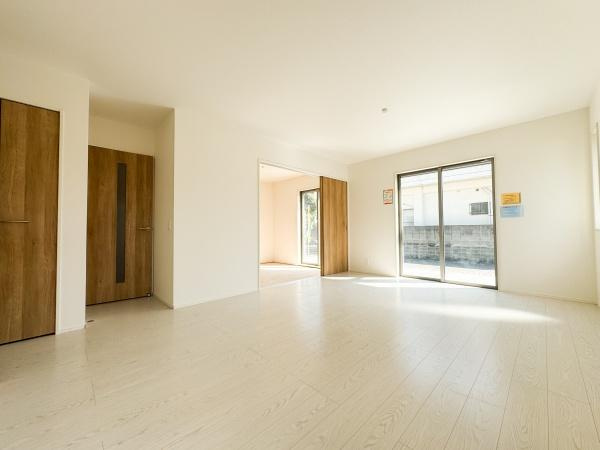 小中島3丁目1期1号棟の居間・リビング|広々としたリビングは明るい日差しがしっかりと入る空間です。白を基調とした床と壁がお部屋をすっきりと見せています。木目調の引き戸がアクセントになり温かみのある印象を与えます。