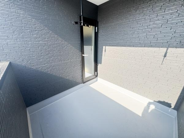 大字光吉5期1号棟のバルコニー|シンプルなデザインのバルコニーで壁面の質感が印象的です。出入りしやすいドアが設置されています。日差しがしっかりと入る空間です。衣類を干すための金具も設置されています。床面はお手入れのしやすい仕様です。