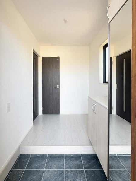 大字光吉5期1号棟の玄関|玄関は明るく開放感のある空間です。大きな鏡付きの収納も設置され使い勝手に配慮されています。シンプルなデザインがすっきりとした印象を与えます。タイルフロアと木目調の床の組み合わせが上品です。