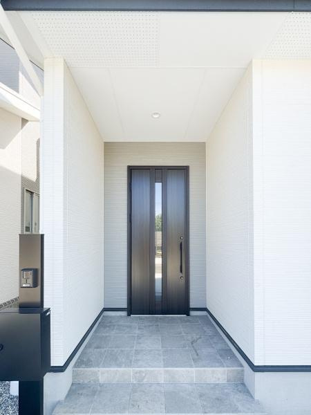 大字小池原1期2号棟の玄関|シンプルなデザインの玄関は落ち着きのある雰囲気を演出しています。ゆとりのあるスペースで出入りも快適です。モダンな扉がアクセントになっており印象的な外観を実現しています。