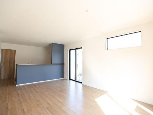 大字光吉4期2号棟の居間・リビング|明るい日差しが差し込むリビング。シンプルな内装でコーディネートもしやすい空間です。木目の床が落ち着いた雰囲気を演出しています。ブルーのアクセント壁が印象的です。開口部からの採光が室内全体に広がります。