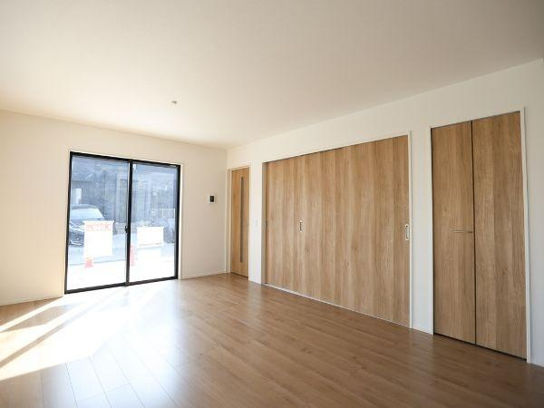 大字光吉4期2号棟の居間・リビング|リビングは大きな窓から自然光が差し込み明るい雰囲気が広がります。木目調の扉とフローリングが調和しすっきりとした印象です。壁面収納も充実しており整理整頓にも便利です。