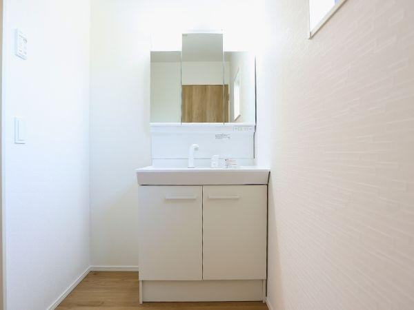 大字光吉4期2号棟の独立洗面台|シンプルで清潔感のある洗面台が設置されています。鏡が大きく毎日の身だしなみも整えやすい空間です。白を基調とした落ち着いたデザインで明るい印象が特徴です。収納スペースもありすっきりと使いやすい仕様です。