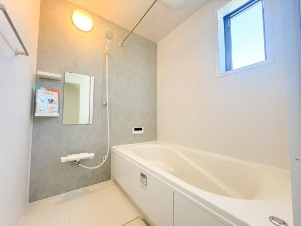 大字小池原1期1号棟の浴室|窓付きで自然光が入るバスルームです。白を基調とした明るい空間が特徴です。壁際の収納スペースも設置されています。ゆったりとした浴槽も完備されています。