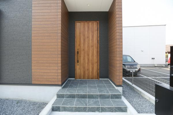 横尾東町1丁目1期2号棟の玄関|スタイリッシュな玄関ドアが住まい全体の雰囲気を引き立てます。広めのアプローチで開放感があります。タイル敷きのステップがアクセントとなっています。