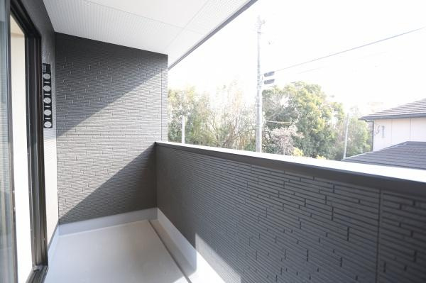 横尾東町1丁目1期2号棟のバルコニー|落ち着いた色合いの外壁がスタイリッシュな印象を与えるバルコニーです。手入れがしやすそうな床材と外からの視線を程よく遮る壁構造が採用されています。窓が大きく室内との行き来もスムーズに行えます。