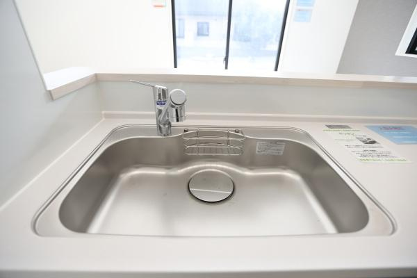 横尾東町1丁目1期2号棟のキッチン|広々としたシンクが設置されています。シンプルなデザインで清潔感があります。カウンター越しに開放感も感じられます。蛇口は洗練されたスタイルです。窓からの光も入り明るい印象です。