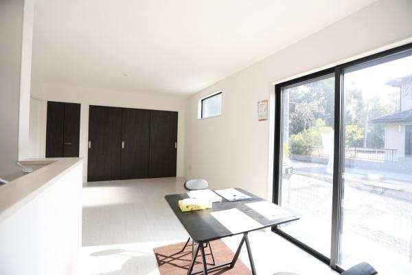 横尾東町1丁目1期2号棟の居間・リビング|リビングは大きな窓から自然光がたっぷり入る明るい空間です。白を基調とした内装が広々とした印象を与えます。隣接するキッチンが使いやすいレイアウトです。室内はすっきりとした仕上がりになっています。