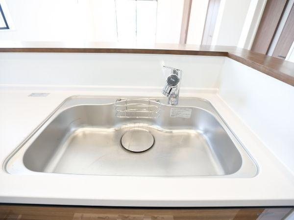 挾間町下市2期8号棟のキッチン|明るい窓と換気扇が設置されたキッチンです。木目調の引き出し収納が充実しており作業スペースも広々としています。シンプルで清潔感のあるデザインが魅力です。床の色合いとキッチンの一体感も印象的です。